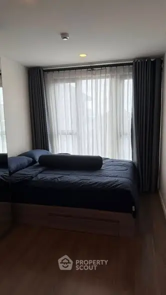 Cozy bedroom with large window and modern decor, featuring dark curtains and a comfortable bed.