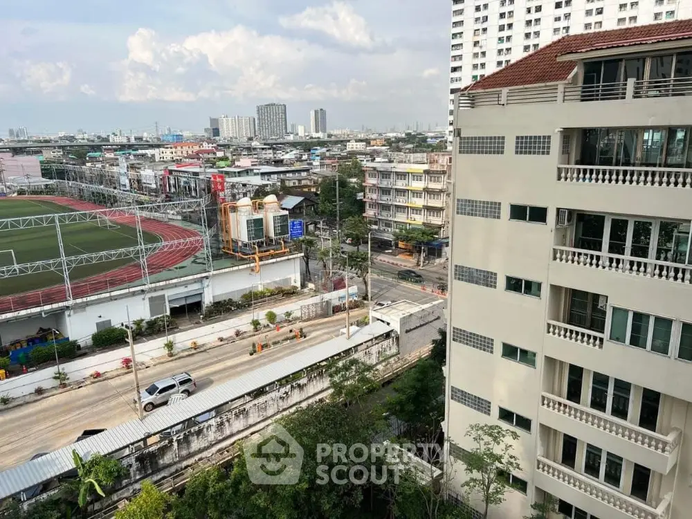 Stunning cityscape view from high-rise building balcony overlooking urban landscape and sports field.