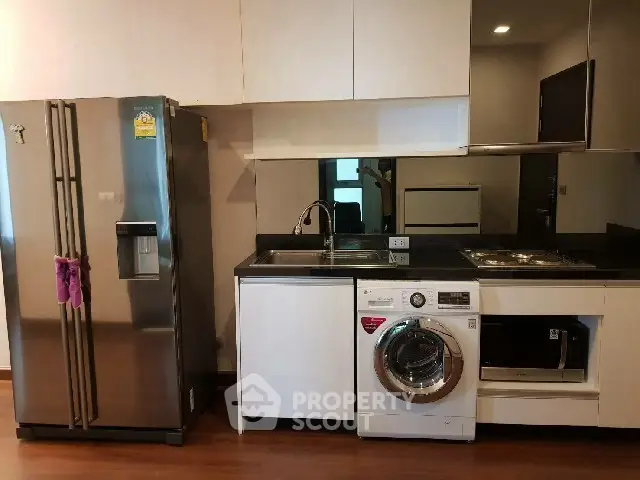 Modern kitchen with stainless steel fridge, washing machine, and sleek cabinetry.