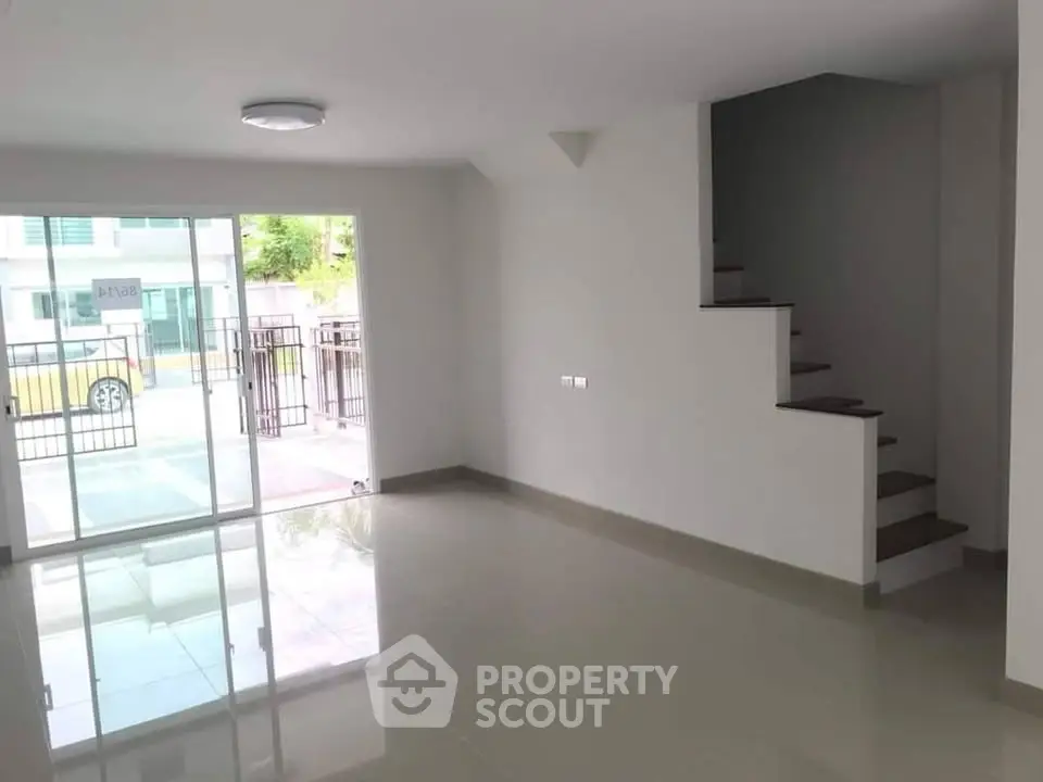 Spacious modern living room with staircase and large glass doors leading to a patio.