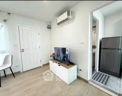 Modern living room with air conditioning and sleek TV setup, adjacent to a compact kitchen and bathroom.