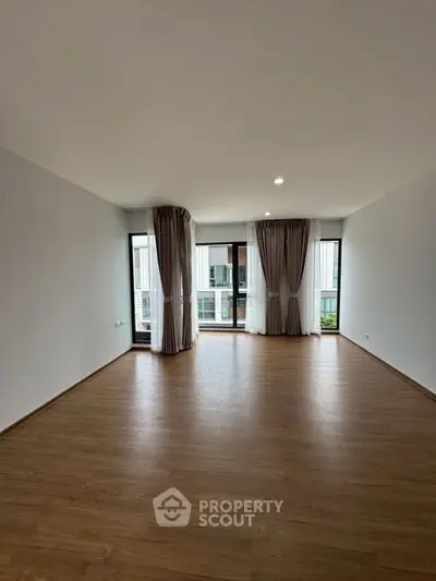 Spacious empty living room with large windows and wooden flooring in modern apartment.