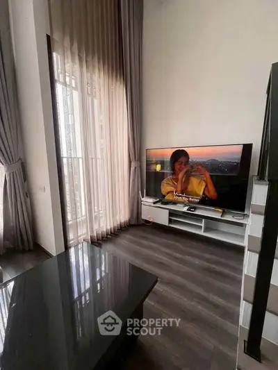 Modern living room with high ceilings and large TV, elegant curtains, and sleek flooring.
