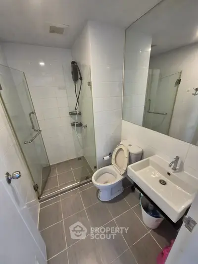 Modern bathroom with glass shower, toilet, and sink in sleek white and gray design.