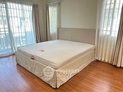 Spacious bedroom with large windows and natural light, featuring a comfortable bed and elegant curtains.