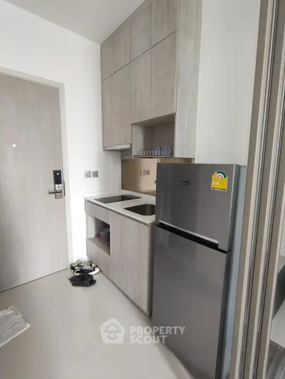 Modern compact kitchen with sleek cabinetry and stainless steel fridge in a stylish apartment.