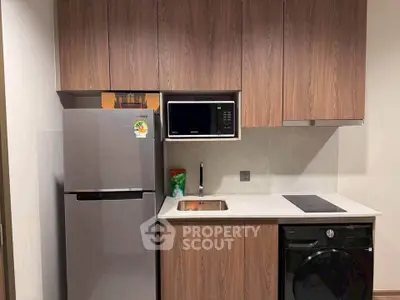 Modern kitchen with sleek appliances and wooden cabinetry, featuring a fridge, microwave, and washing machine.