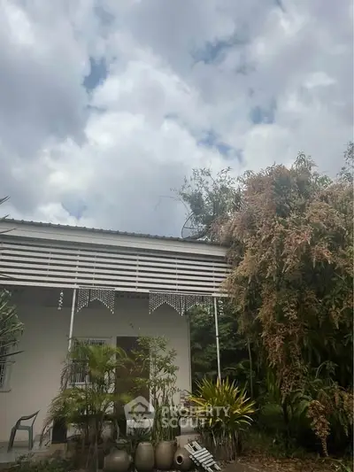Charming exterior view of a cozy home surrounded by lush greenery and a cloudy sky.