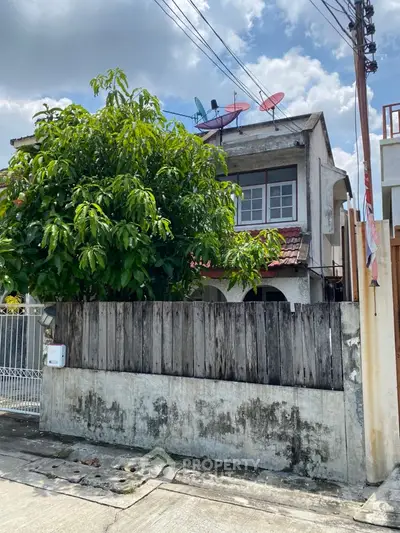 Charming two-story house with rustic wooden fence and lush greenery in a suburban neighborhood.