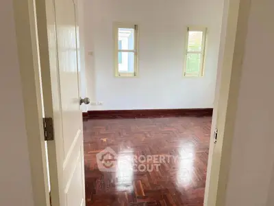 Spacious empty room with polished wooden floors and two windows, perfect for customization.