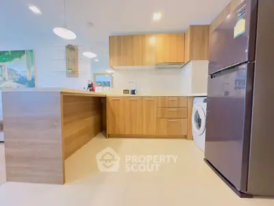 Modern kitchen with wooden cabinets, fridge, and washing machine in open layout.