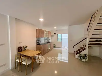 Modern open-plan kitchen and dining area with sleek staircase and bright lighting.