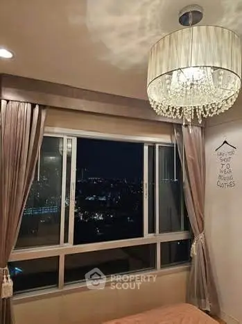 Elegant bedroom with city view, featuring a luxurious chandelier and large window for stunning night vistas.
