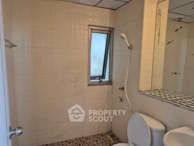 Cozy bathroom with tiled walls and floor, featuring a shower and window for natural light.