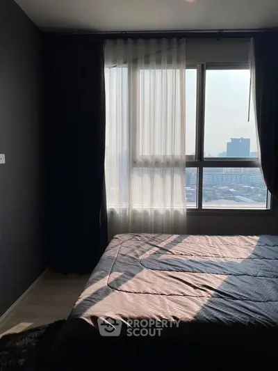 Cozy bedroom with large window offering city view and natural light, perfect for relaxation.