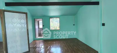 Spacious room with teal walls and wooden flooring, featuring a decorative glass door and natural light.