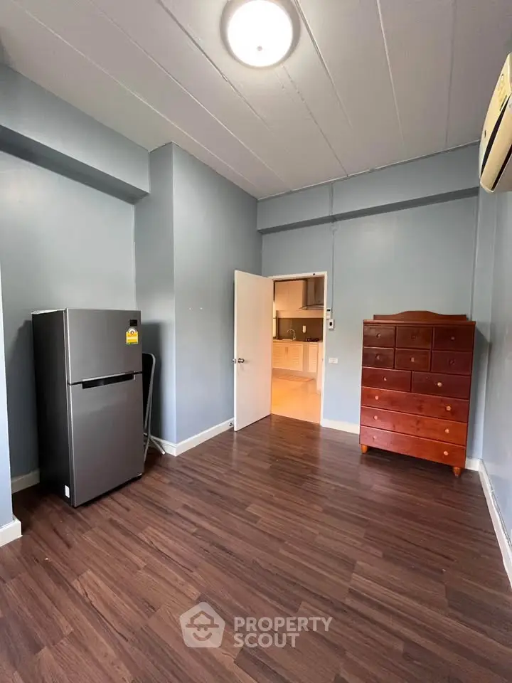 Spacious room with wooden flooring, featuring a fridge and chest of drawers, ideal for versatile use.