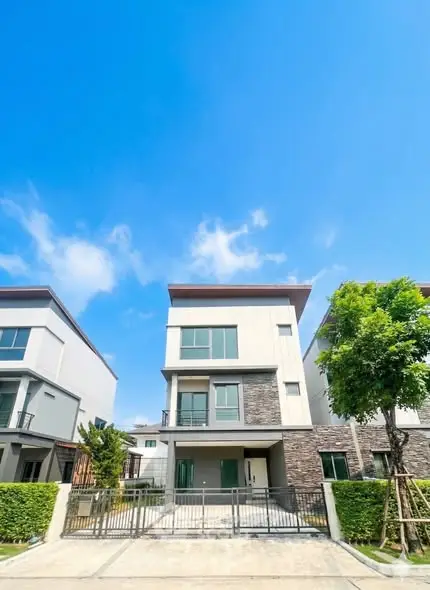 Modern three-story townhouse with sleek design and lush greenery under a clear blue sky.