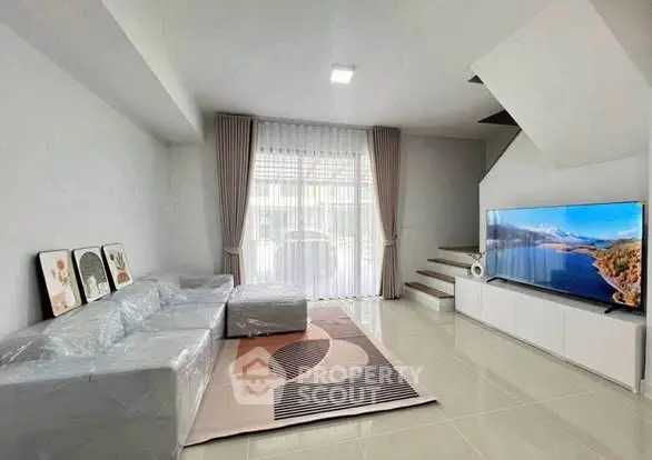 Modern living room with sleek design, large TV, and natural light from window.