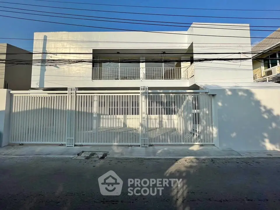 Modern minimalist white house exterior with gated entrance and balcony, showcasing sleek architectural design.