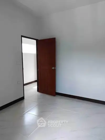 Spacious empty room with open wooden door and bright tiled floor.