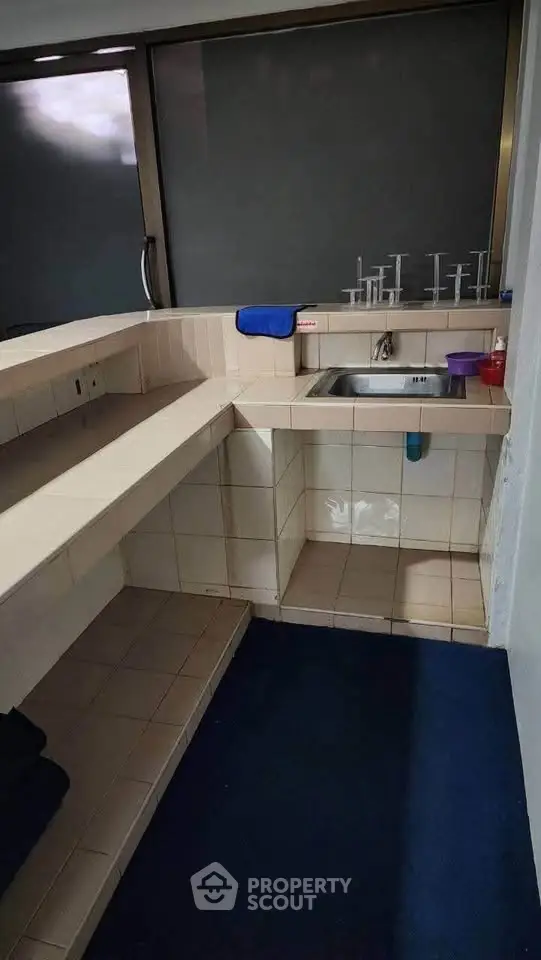Compact kitchen with tiled countertops and stainless steel sink in modern apartment.