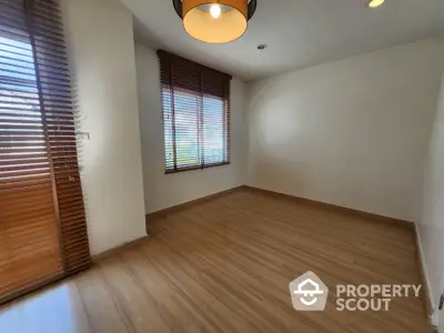 Spacious empty room with wooden flooring and large windows with blinds