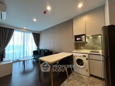 Modern living room with integrated kitchen featuring washing machine and sleek furniture.