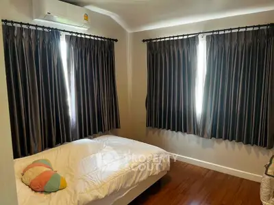 Cozy bedroom with wooden flooring and natural light through elegant curtains.