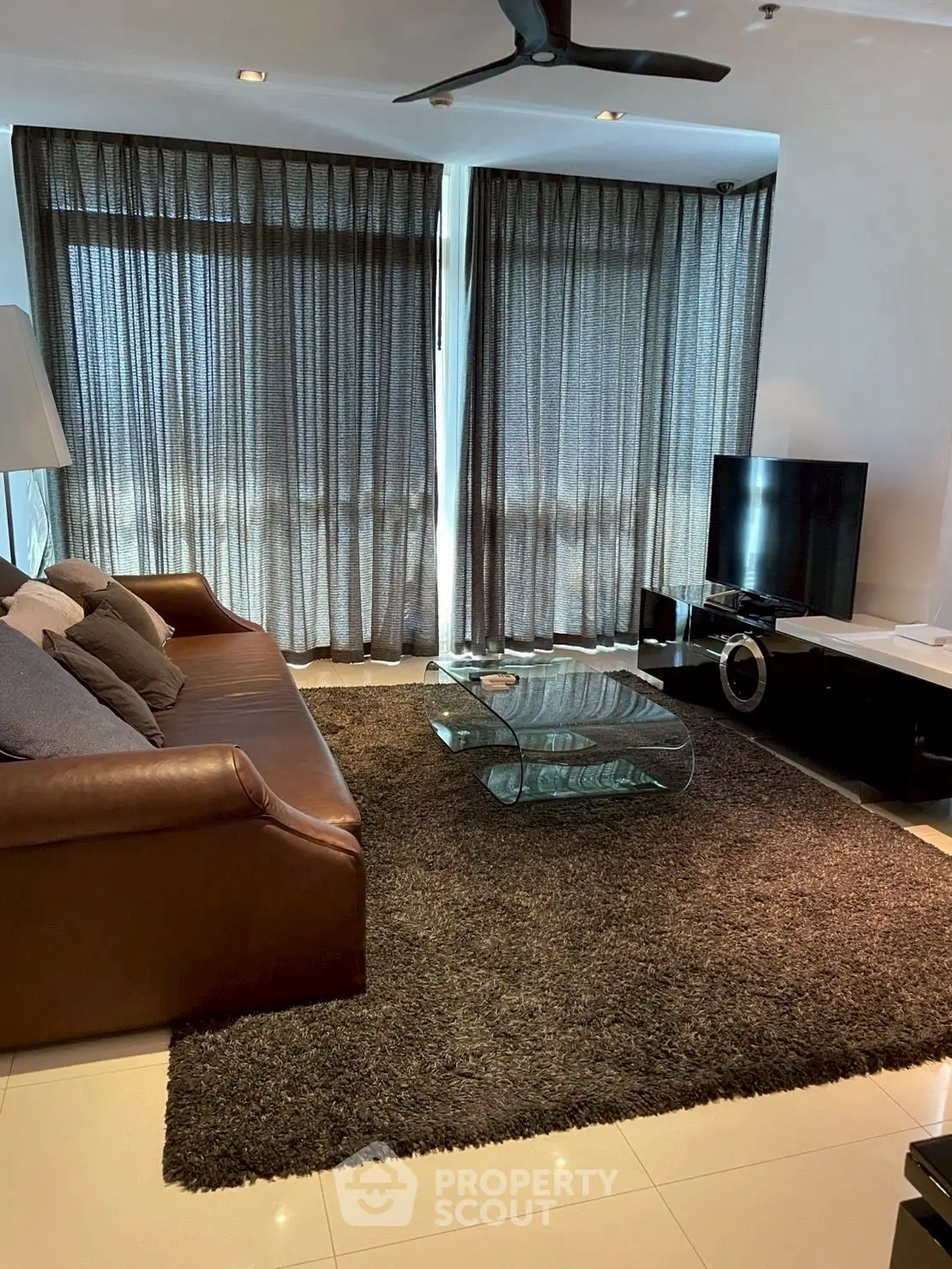 Modern living room with leather sofa, glass coffee table, and large TV setup.