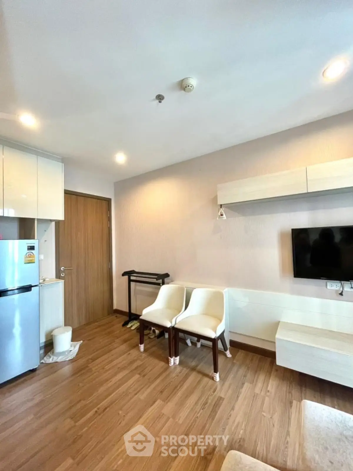 Modern living room with wooden flooring, wall-mounted TV, and compact kitchen area.