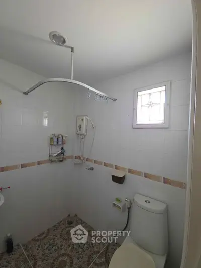 Compact bathroom with shower and toilet, featuring tiled walls and floor, small window for natural light.
