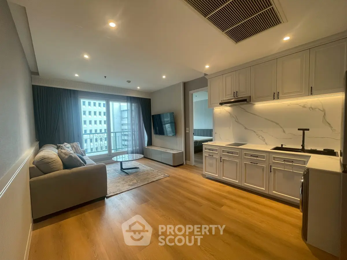 Modern open-layout living room with kitchen, featuring sleek cabinetry and large window with city view.