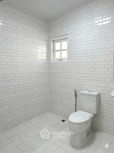 Minimalist white tiled bathroom with window and modern toilet design.