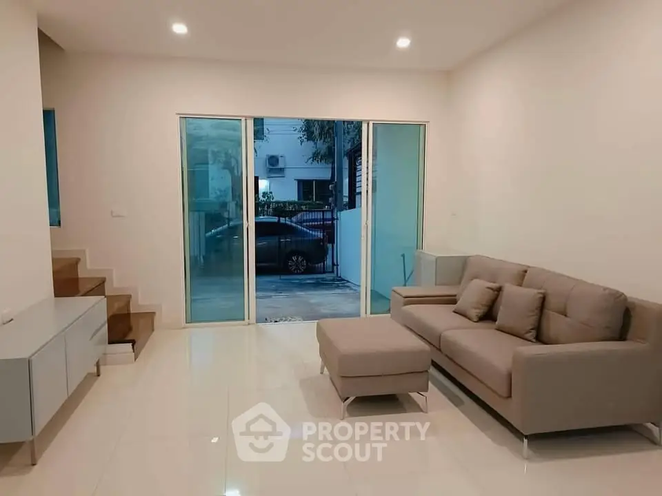 Spacious modern living room with sleek sofa and large glass doors leading to outdoor area.