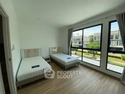 Spacious bedroom with twin beds and large windows offering a serene view of the neighborhood.