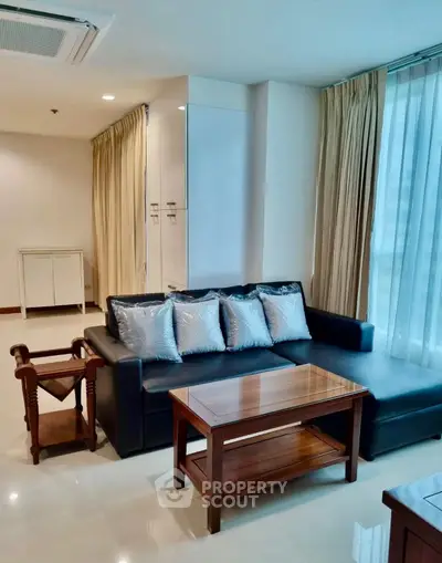 Modern living room with sleek black sofa and elegant wooden coffee table, featuring floor-to-ceiling windows.
