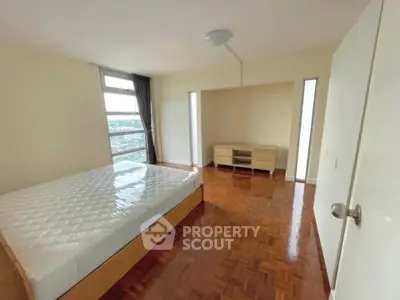 Spacious bedroom with parquet flooring and large window offering city views.