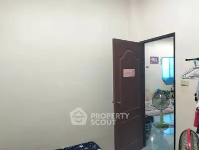 Simple bedroom with open door leading to another room, minimal decor.