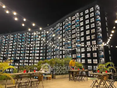 Stunning night view of modern apartment building with outdoor dining area and string lights.