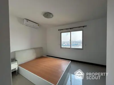 Spacious bedroom with large window offering stunning city view and modern air conditioning unit.