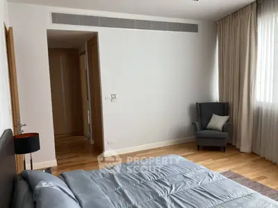 Spacious bedroom with elegant decor and natural light, featuring a cozy armchair and modern design.