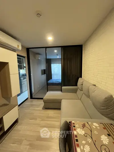 Modern living room with cozy sectional sofa and view into bedroom through glass partition.