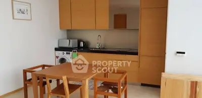 Modern kitchen with wooden cabinets and dining area, featuring a washing machine and microwave.