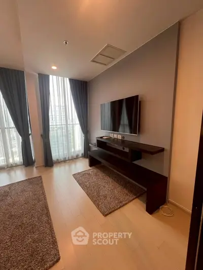 Modern living room with sleek TV setup and large windows offering city views.