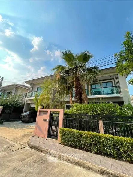 Modern two-story house with lush greenery and palm tree in front yard, under a clear blue sky.