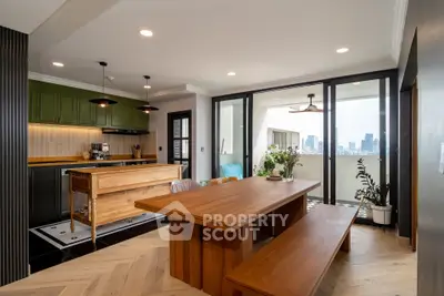 Modern kitchen with open layout and city view balcony, featuring wooden dining table and green cabinets.