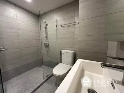 Sleek modern bathroom with glass shower enclosure, large mirror, and elegant gray tiling, perfect for contemporary living.