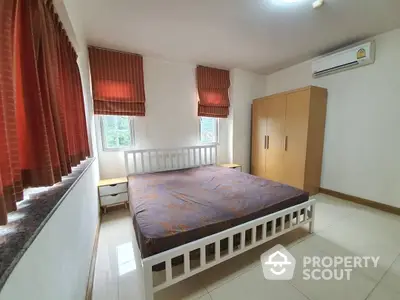 Spacious bedroom with large windows, red curtains, and air conditioning, featuring a king-sized bed and ample wooden wardrobe.