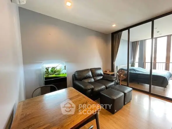 Modern living room with leather sofa and aquarium, adjacent to a bedroom with glass partition.